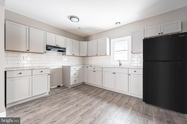 kitchen featuring light hardwood / wood-style floors, black refrigerator, and white cabinetry