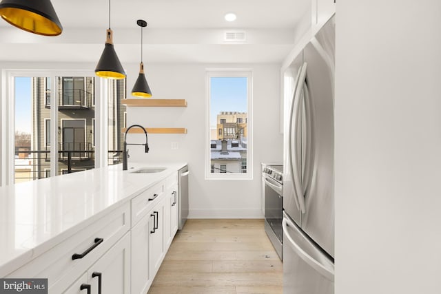 kitchen with white cabinetry, appliances with stainless steel finishes, pendant lighting, light stone counters, and sink