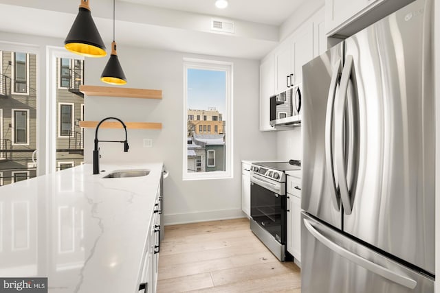 kitchen with light stone countertops, pendant lighting, appliances with stainless steel finishes, white cabinetry, and sink