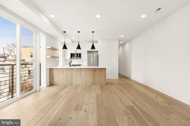 kitchen with light wood-type flooring, appliances with stainless steel finishes, sink, and pendant lighting