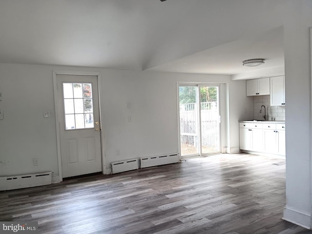 unfurnished living room with baseboard heating, wood-type flooring, and sink