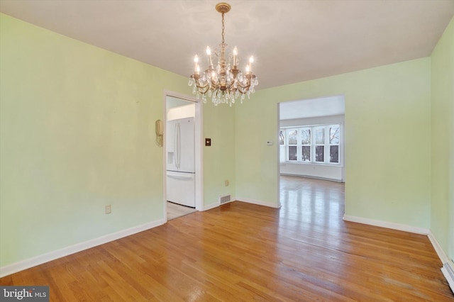 spare room featuring a chandelier and light hardwood / wood-style flooring