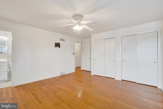 unfurnished bedroom featuring ceiling fan, two closets, connected bathroom, and light hardwood / wood-style floors