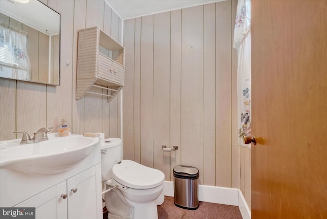 bathroom with toilet, wood walls, and vanity