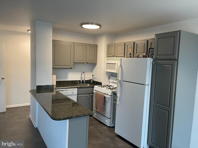 kitchen featuring sink, kitchen peninsula, dark stone counters, and white appliances