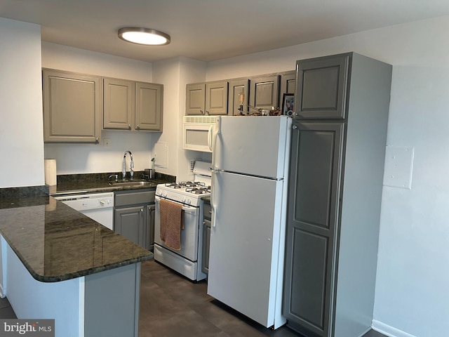 kitchen featuring sink, white appliances, kitchen peninsula, and dark stone countertops