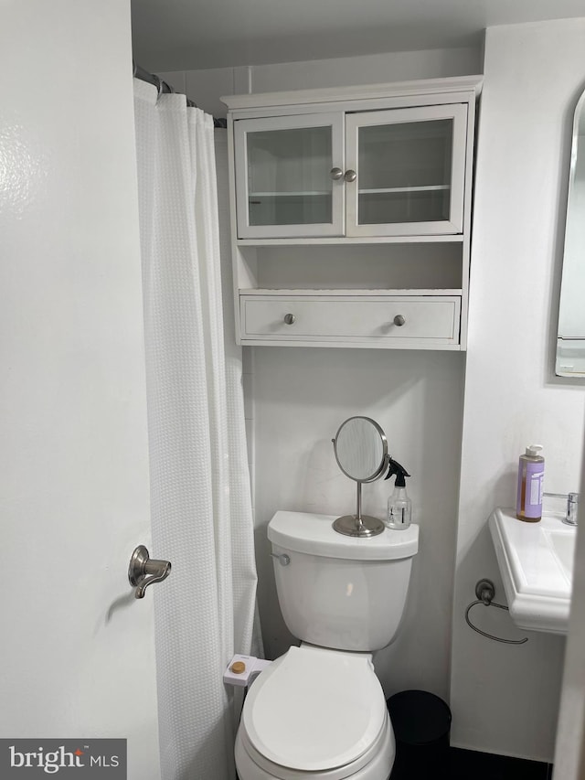 bathroom featuring toilet, a shower with shower curtain, and sink