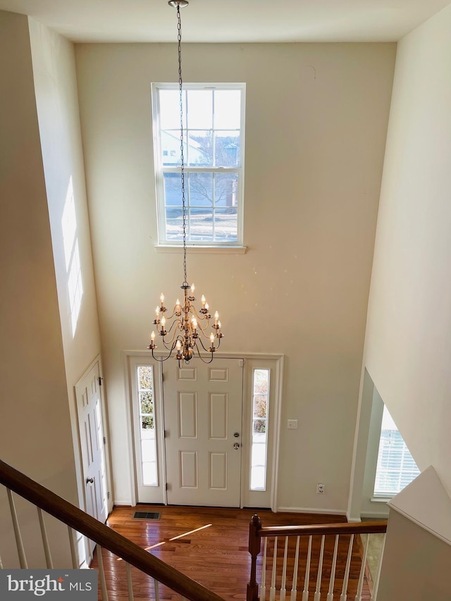 foyer with a high ceiling, wood-type flooring, a healthy amount of sunlight, and an inviting chandelier