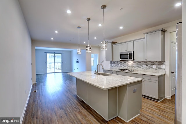 kitchen with gray cabinets, stainless steel appliances, pendant lighting, light stone counters, and sink