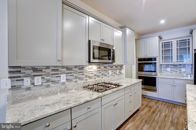 kitchen featuring light stone counters, backsplash, appliances with stainless steel finishes, and light hardwood / wood-style flooring