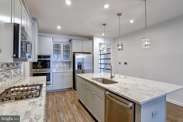 kitchen with a center island with sink, decorative backsplash, sink, hanging light fixtures, and appliances with stainless steel finishes