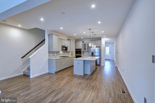 kitchen featuring backsplash, light hardwood / wood-style floors, a center island, pendant lighting, and stainless steel appliances