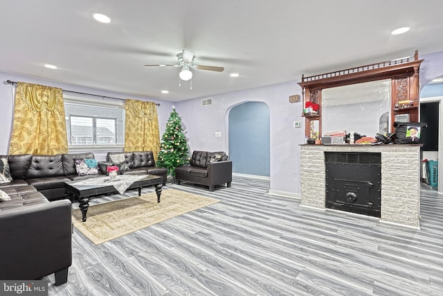 living room featuring a brick fireplace, light wood-type flooring, and ceiling fan