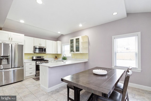 kitchen featuring baseboards, appliances with stainless steel finishes, glass insert cabinets, a peninsula, and a sink