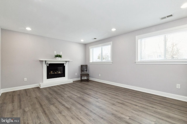 unfurnished living room with a fireplace with raised hearth, wood finished floors, visible vents, and baseboards