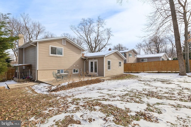 snow covered rear of property featuring french doors, fence, a chimney, and a patio