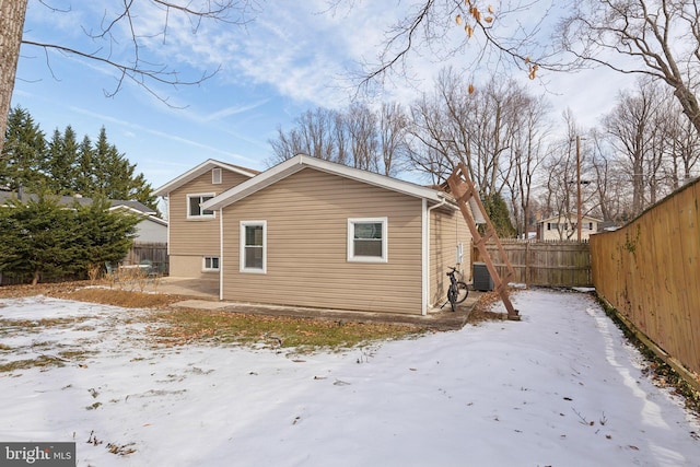 view of snowy exterior featuring cooling unit and a fenced backyard