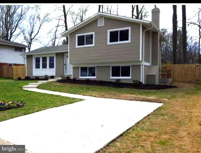 tri-level home featuring a chimney, fence, and a front yard