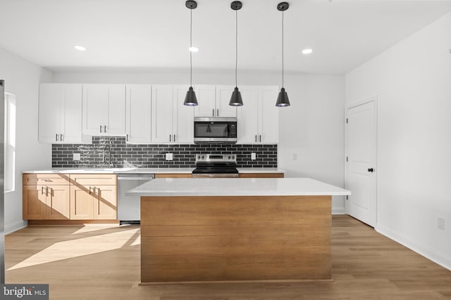 kitchen with decorative light fixtures, white cabinets, light hardwood / wood-style floors, a kitchen island, and appliances with stainless steel finishes