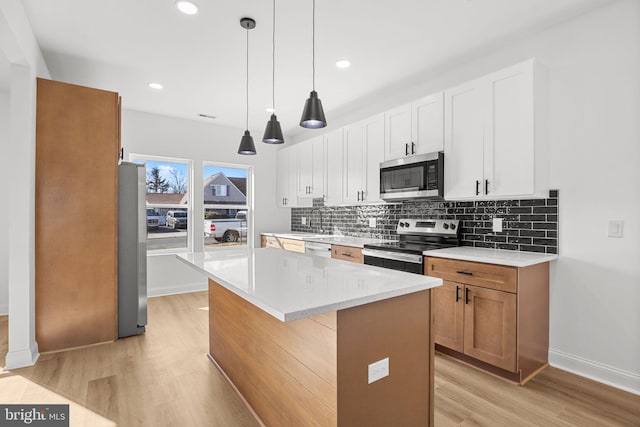 kitchen featuring appliances with stainless steel finishes, a center island, light stone countertops, pendant lighting, and white cabinetry