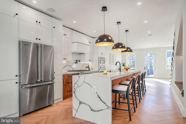 kitchen with decorative light fixtures, white cabinetry, stainless steel appliances, a kitchen island with sink, and light parquet floors