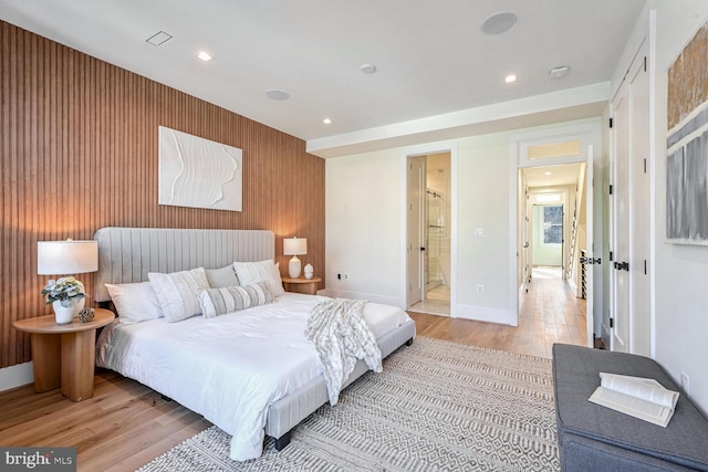 bedroom featuring light hardwood / wood-style flooring, ensuite bath, and wooden walls