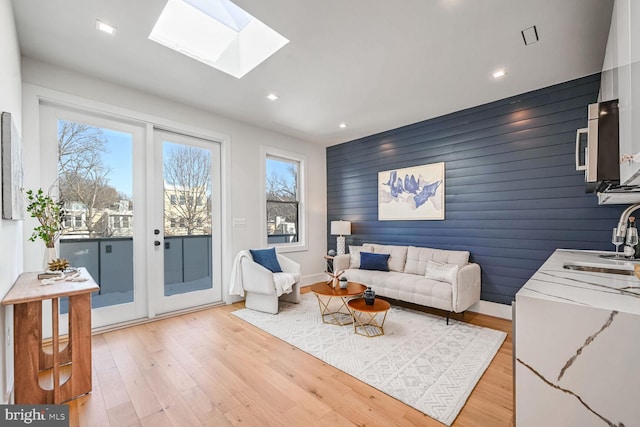 living room featuring wood walls, light hardwood / wood-style flooring, and a skylight