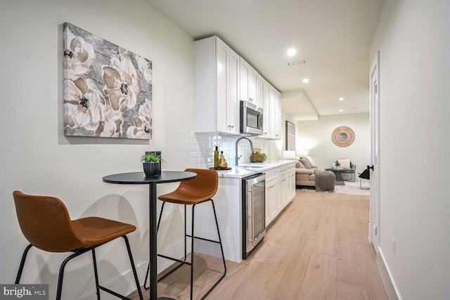 kitchen with wine cooler, decorative backsplash, sink, white cabinetry, and light hardwood / wood-style flooring