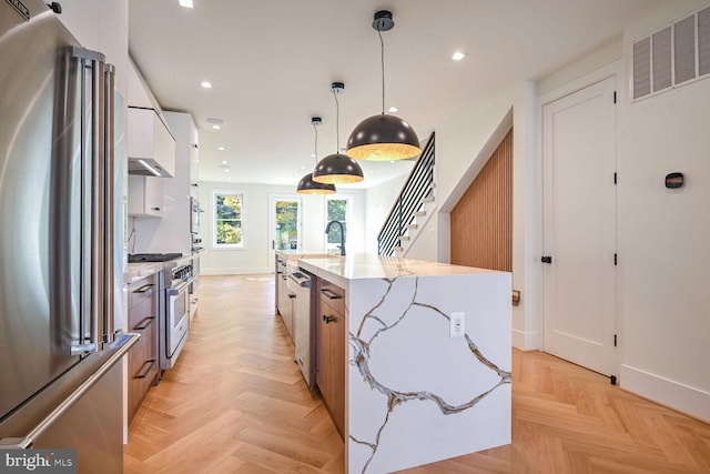 kitchen featuring decorative light fixtures, light parquet floors, an island with sink, white cabinets, and high quality appliances