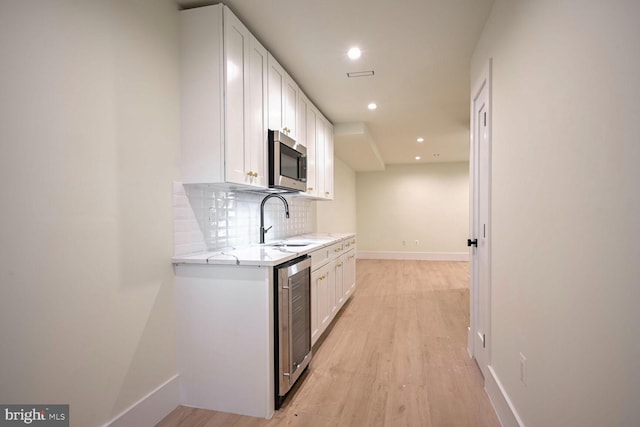 kitchen with white cabinetry, backsplash, light wood-type flooring, light stone counters, and sink