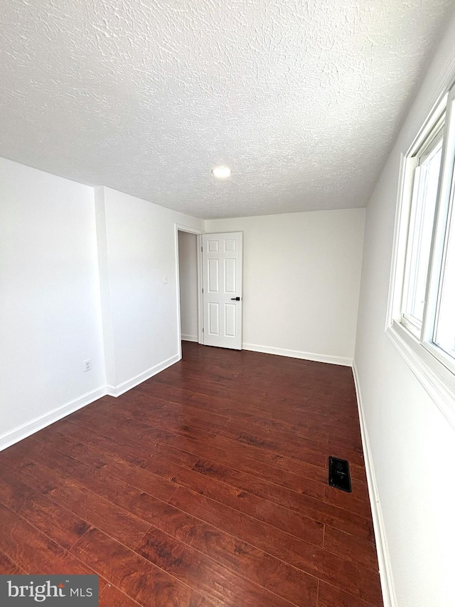 unfurnished room with dark wood-type flooring and a textured ceiling