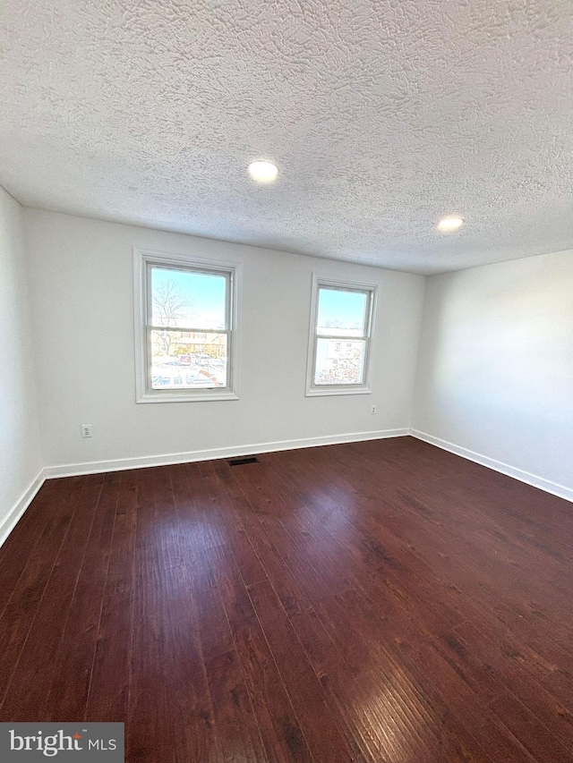 spare room with a textured ceiling and dark hardwood / wood-style floors