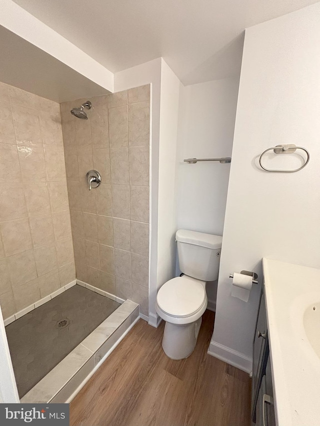 bathroom featuring toilet, wood-type flooring, tiled shower, and vanity