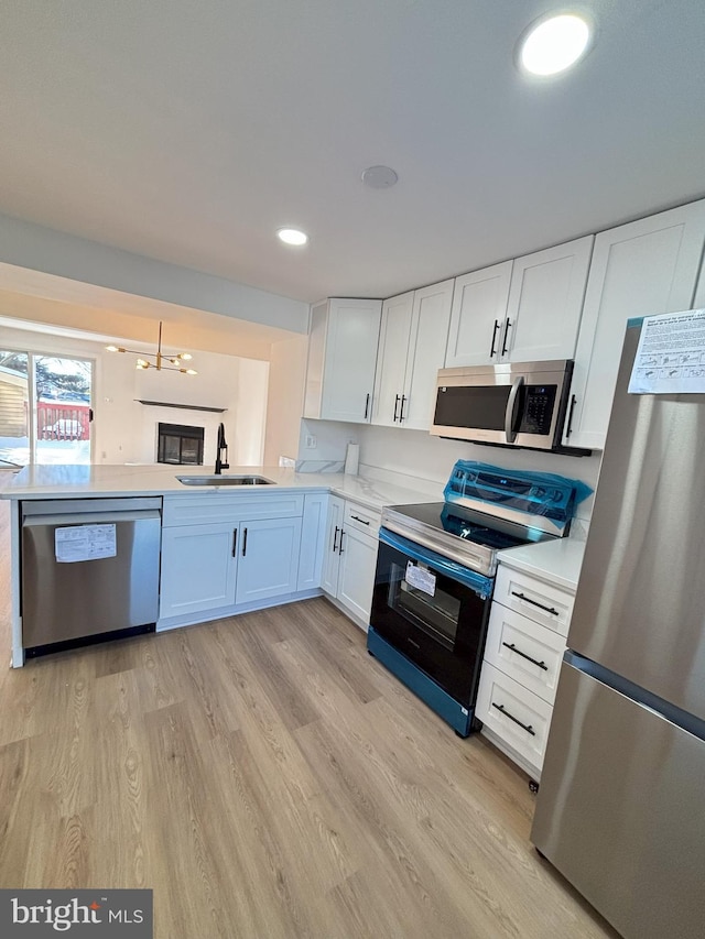 kitchen featuring a notable chandelier, sink, white cabinetry, light wood-type flooring, and stainless steel appliances