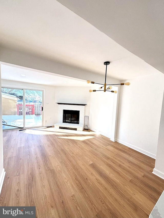 unfurnished living room with a brick fireplace, wood-type flooring, and an inviting chandelier