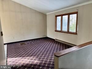 carpeted empty room featuring ornamental molding and a baseboard heating unit