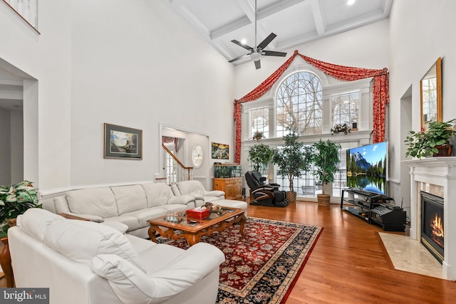 living room with ceiling fan, a fireplace, beamed ceiling, a high ceiling, and coffered ceiling