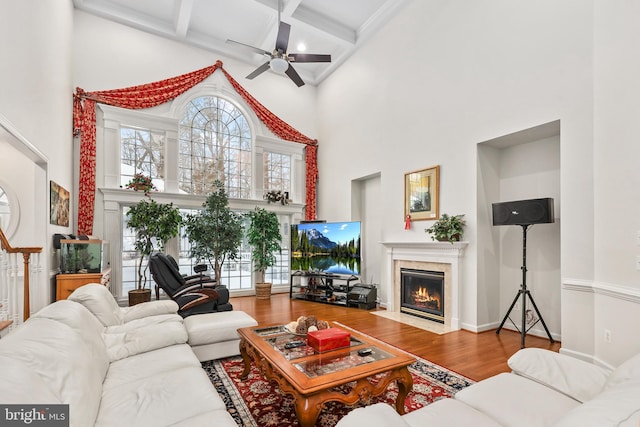 living room featuring ceiling fan, beamed ceiling, a high ceiling, hardwood / wood-style flooring, and a high end fireplace