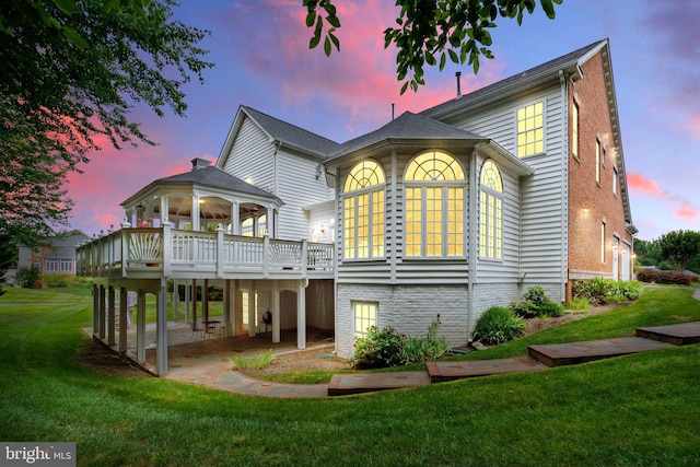 back house at dusk with a deck and a yard