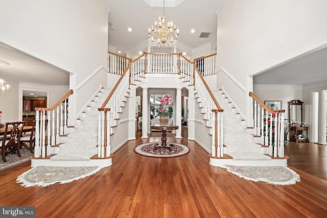 foyer entrance featuring an inviting chandelier, hardwood / wood-style floors, crown molding, and a high ceiling