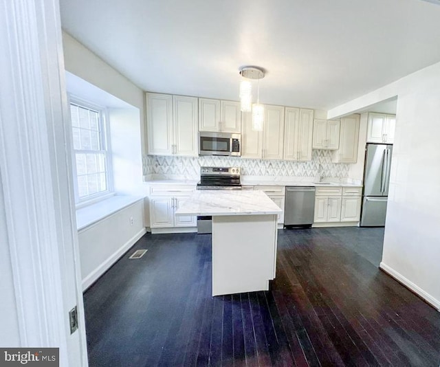 kitchen featuring a kitchen island, decorative backsplash, hanging light fixtures, light stone countertops, and appliances with stainless steel finishes