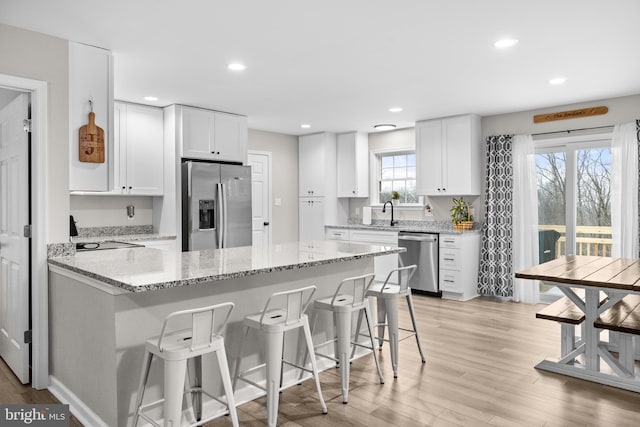 kitchen with white cabinetry, a breakfast bar area, appliances with stainless steel finishes, light hardwood / wood-style flooring, and light stone counters