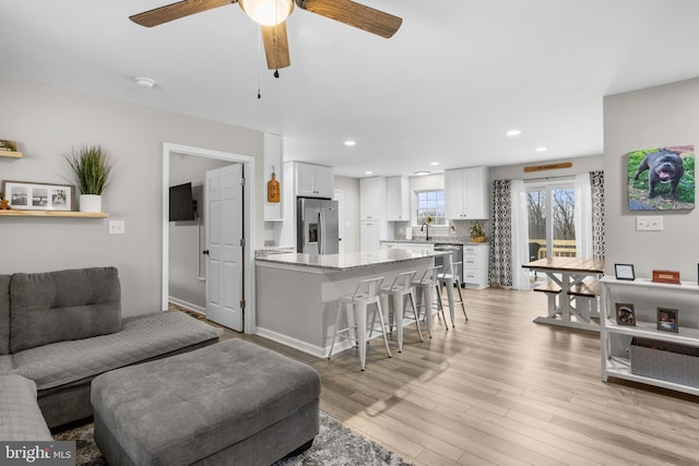 living room with ceiling fan, sink, and light wood-type flooring