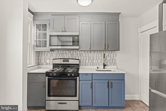 kitchen with light stone countertops, backsplash, appliances with stainless steel finishes, light tile patterned flooring, and sink