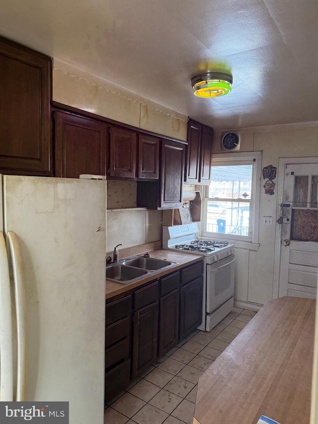 kitchen with light tile patterned floors, sink, dark brown cabinetry, and white appliances