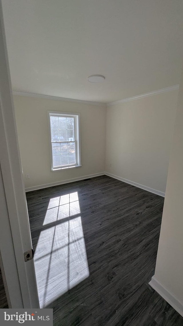 empty room with dark wood-style floors, baseboards, and crown molding