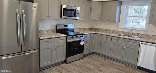 kitchen featuring appliances with stainless steel finishes, light wood-type flooring, gray cabinets, and a sink