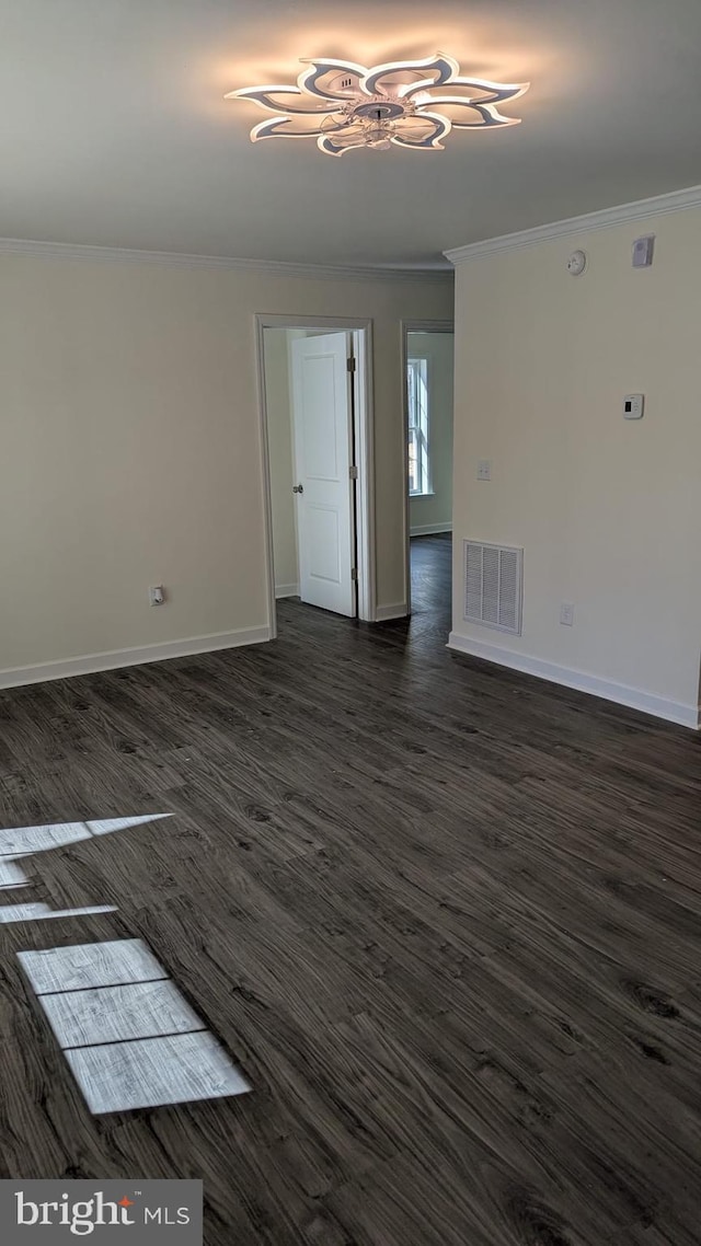 spare room featuring baseboards, visible vents, dark wood-style flooring, and ornamental molding