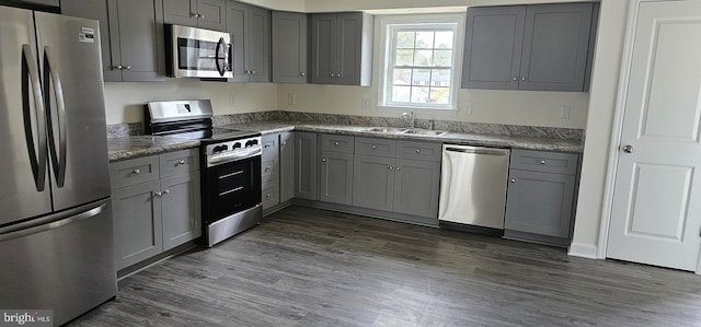 kitchen featuring dark wood-style flooring, appliances with stainless steel finishes, gray cabinets, and a sink