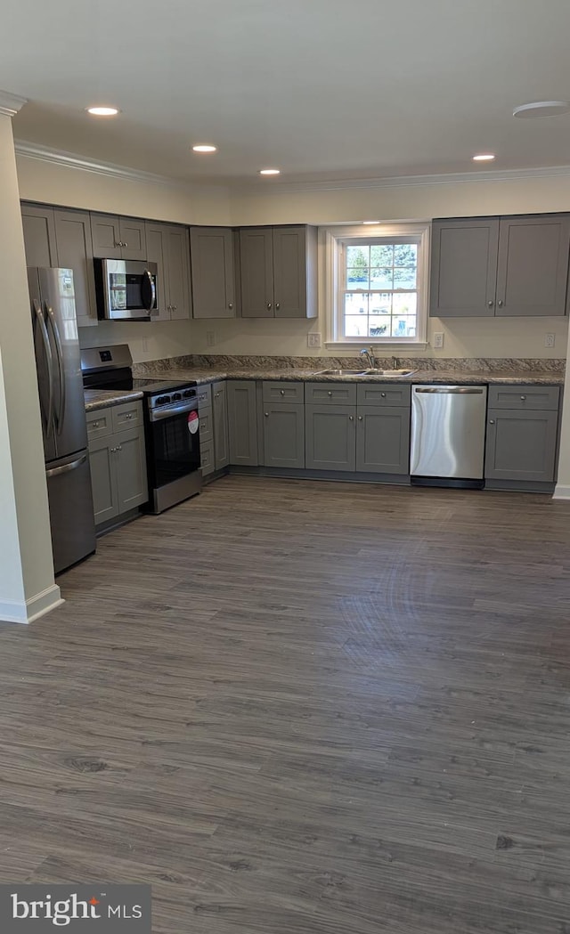 kitchen with stainless steel appliances, a sink, ornamental molding, gray cabinets, and dark wood-style floors